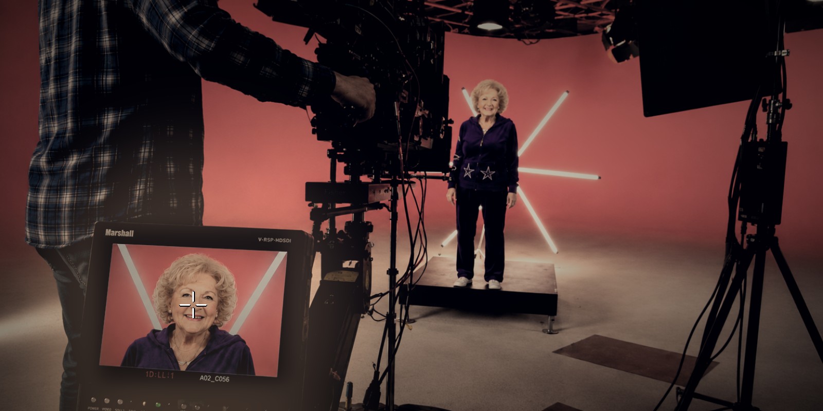 Behind the camera on the Betty White campaign shoot — the operator framing her on the monitor, a centering mark over her face, as she stands lit on the set