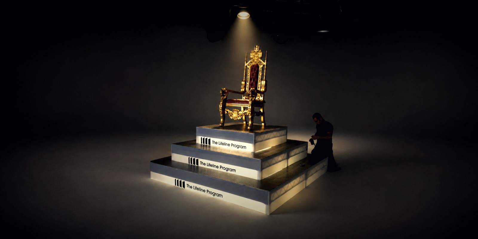 The gilded campaign throne, empty, spotlit atop the illuminated The Lifeline Program pyramid on a darkened soundstage, a crew member working at its base — the seat Betty White made the face of an industry